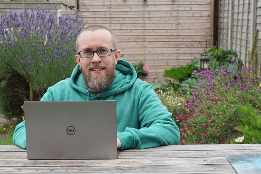 Paul Seward-Prior, BaseKit Operations Engineer, sitting at a garden bench using this laptop