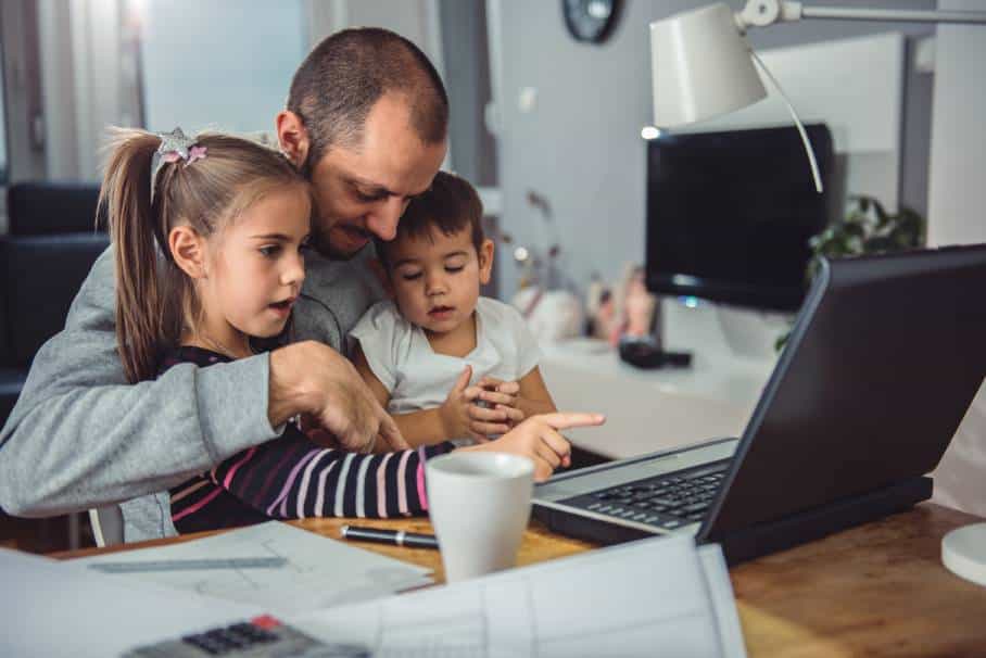 A father working from home in front of laptop with two children sitting on his lap